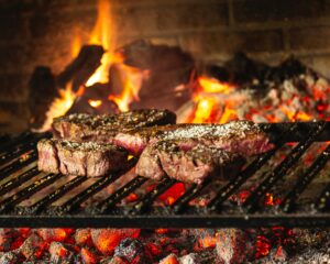 Image of steaks grilling over a charcoal fire