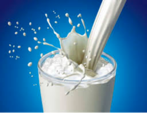 Milk being poured into clear glass with milk splashing out of glass into blue background.