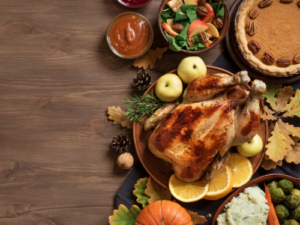 Holiday meal of whole cooked chicken garnished with orange slices and apples surrounded by side dishes and pumpkin pie.