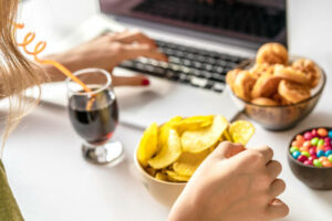 Girl works at a computer and eats unhealthy food. 