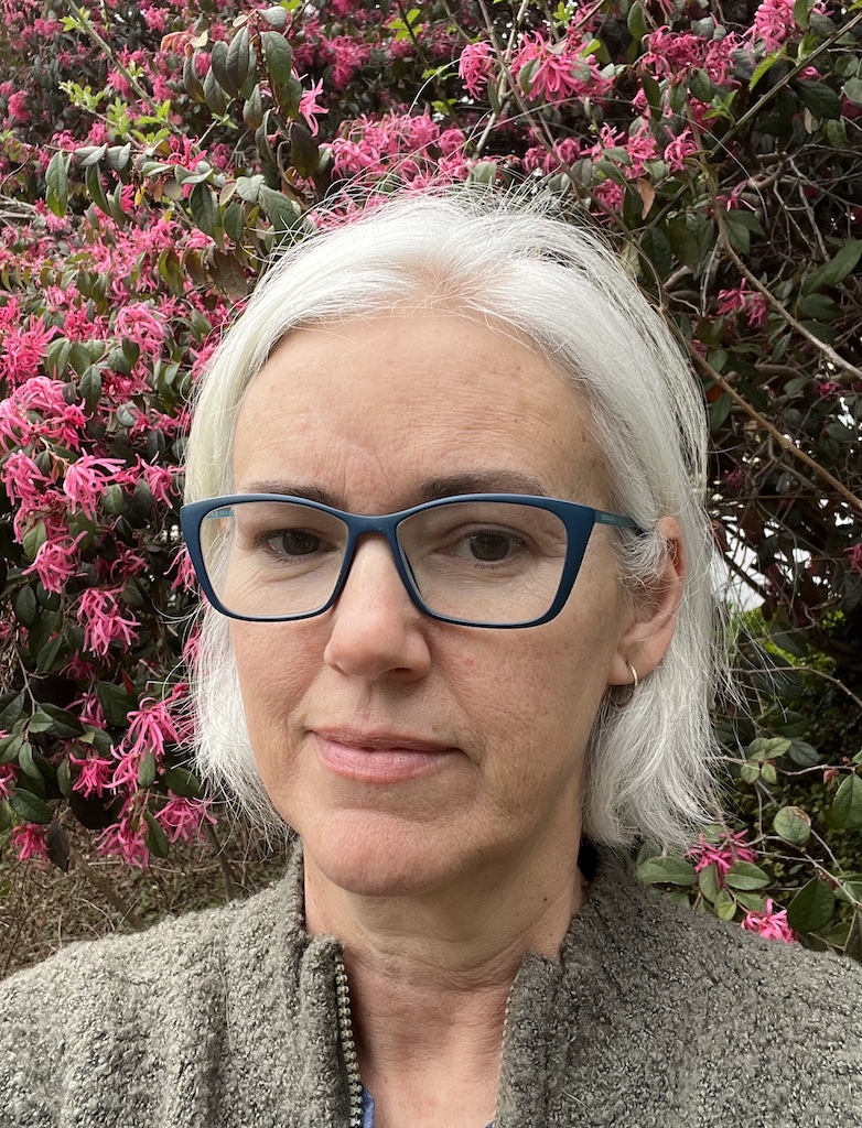 A portrait photograph of a woman in front of a pink flowered bush.